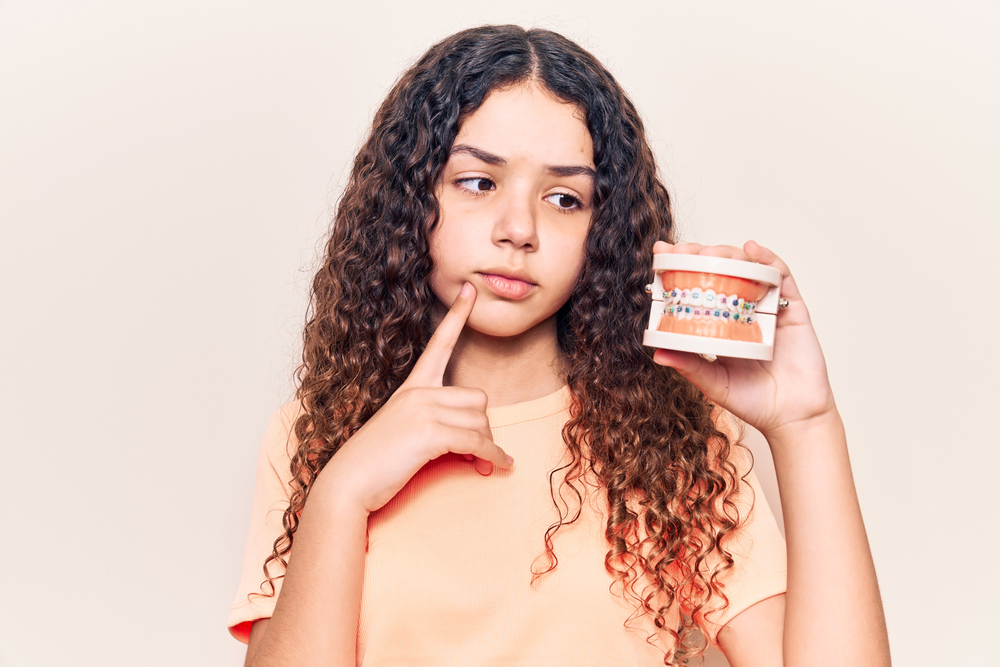 Girl holding a dental model with braces and thinking about teeth care after braces removal