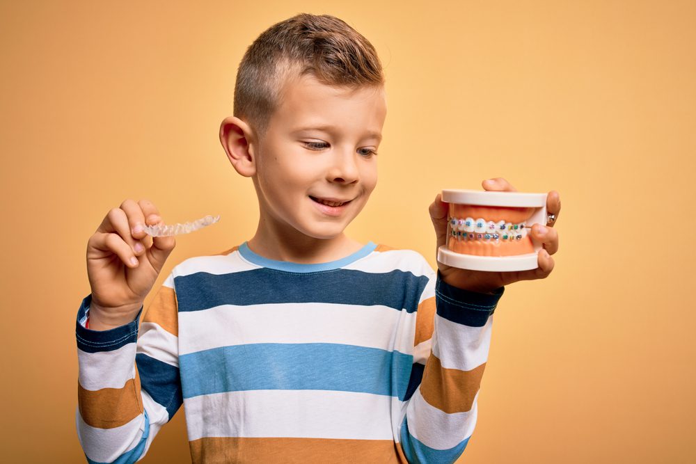 Young boy holding clear aligner and braces model comparing Invisalign and traditional braces for teenagers